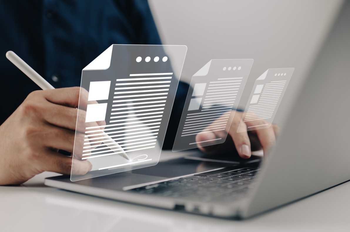 Une personne utilisant un stylet sur un ordinateur portable affichant des documents numériques stylisés en lévitation, illustrant la solution de gestion documentaire HABIGED