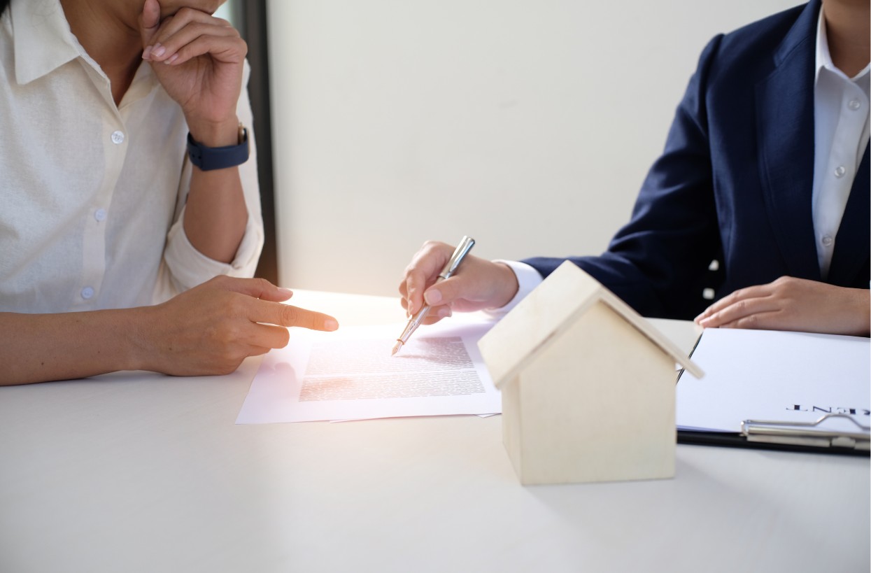 Gros plan sur deux personnes en rendez-vous professionnel autour d'un contrat et d'une maquette de maison, incitant à demander une démonstration de la solution Habiged